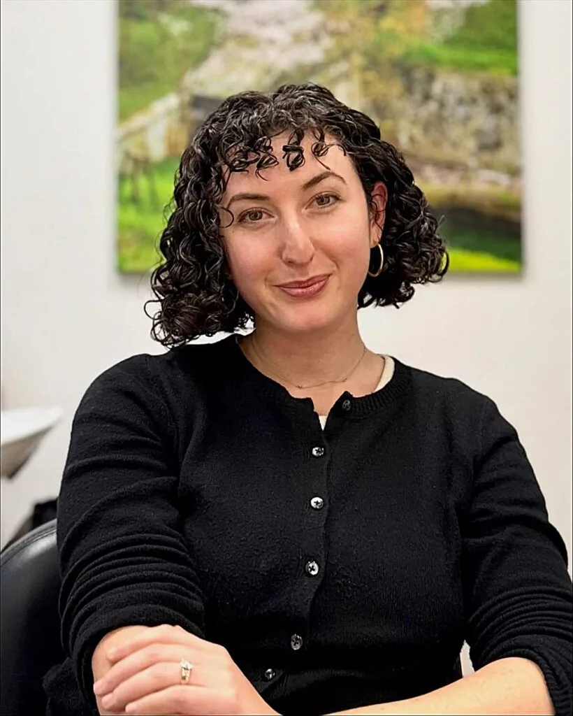 Defined dark curly bob with side part and small hoops
