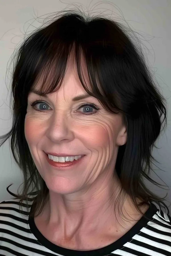 Smiling woman with voluminous curtain bangs and a blowout hairstyle, radiating a youthful appearance.
