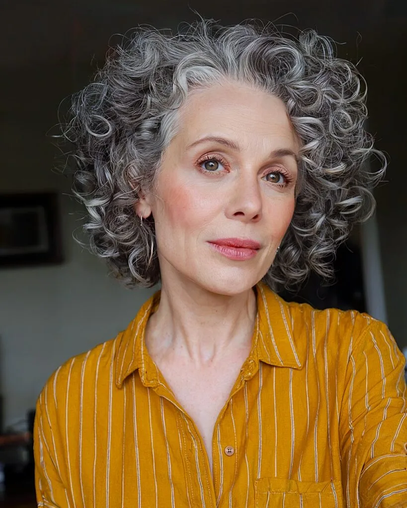 Short voluminous curly gray hairstyle for women over 50 with natural texture and soft layers