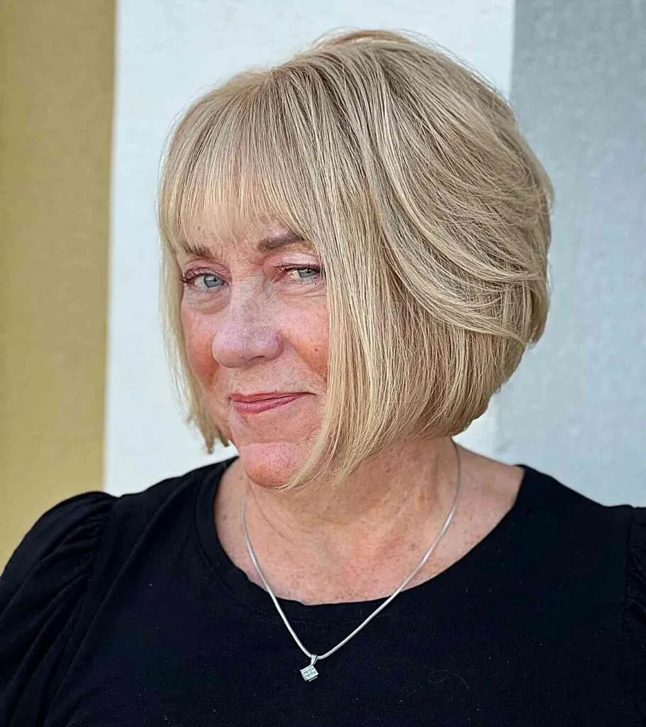 Chin-Grazing Stylish Graduated Blonde Bob with Subtle Bangs for Ladies Over Fifty with Rounded Faces