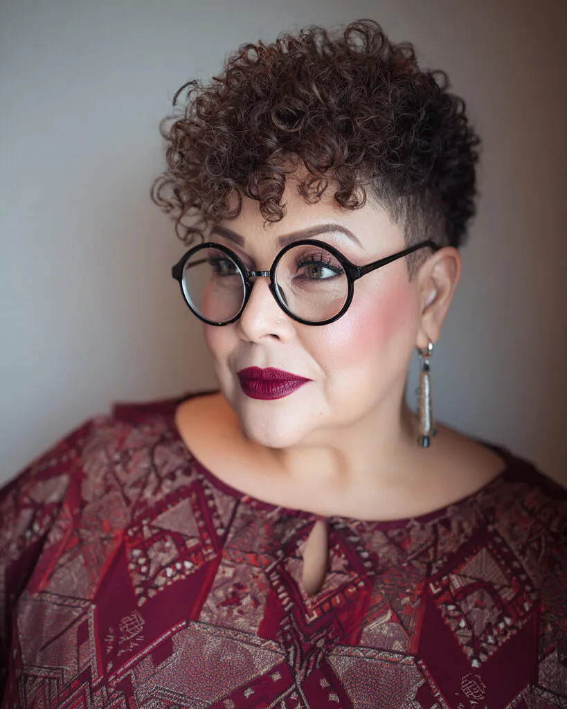 Short curly tapered haircut with undercut sides for women over 50 wearing glasses