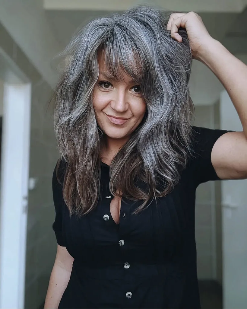 Voluminous layered cut with wispy bangs for grey hair over 50, adding body and soft texture to medium-length strands